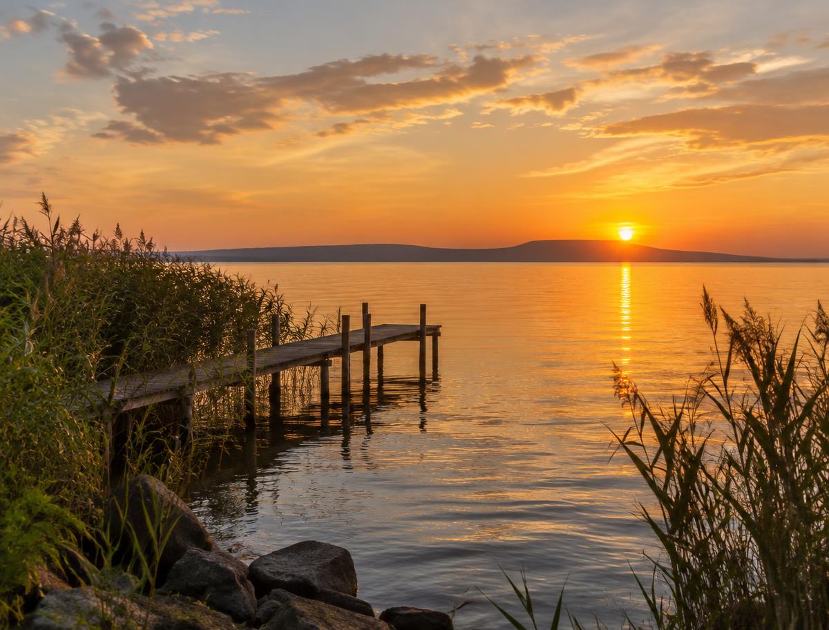 Nyugodt Balaton-part náddal és fa stéggel naplementében
